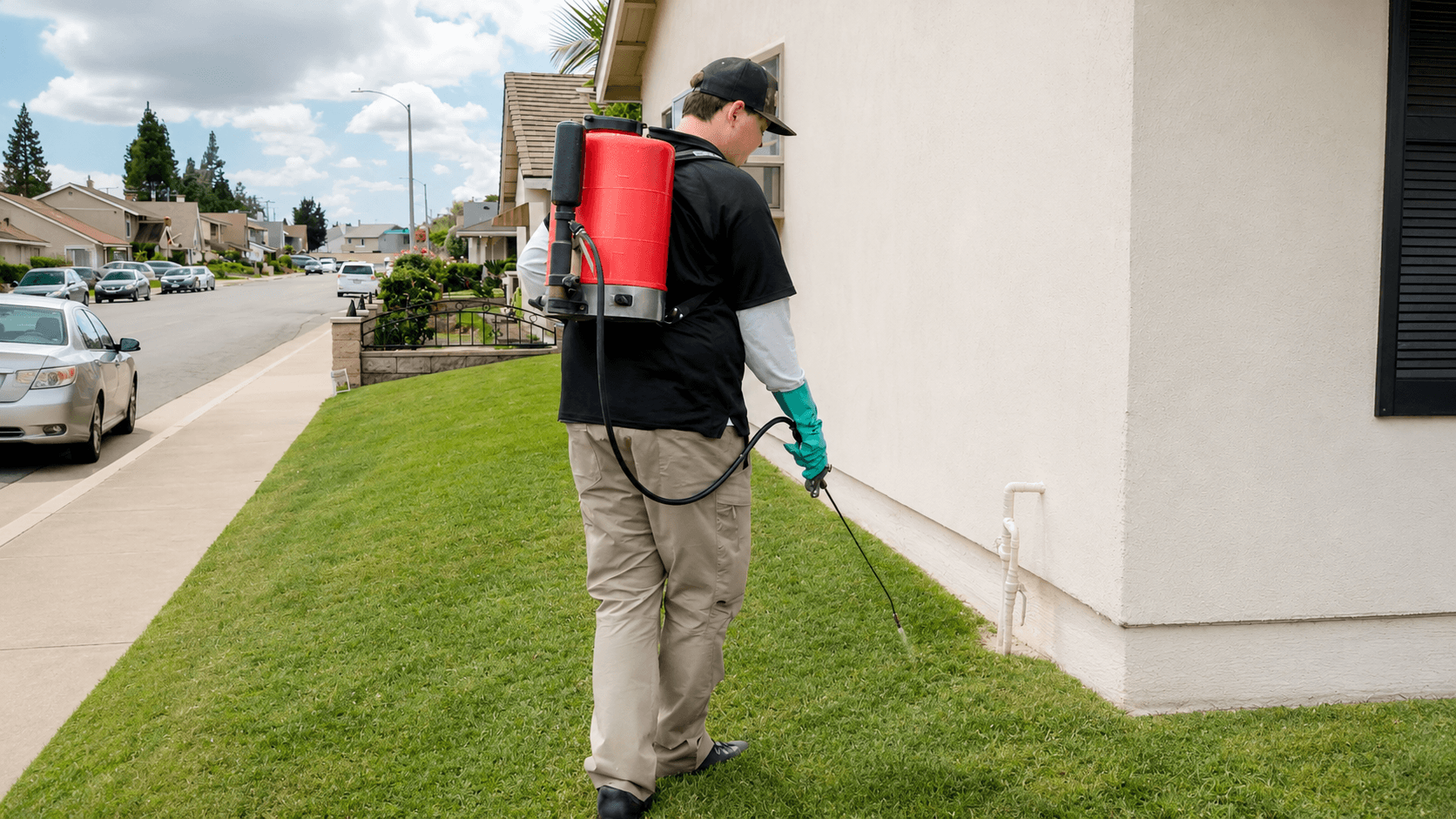 Trident Pest Control technician treating a home exterior with a backpack sprayer